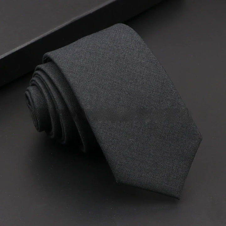 Rolled black plain silk tie on black background with matching black gift box