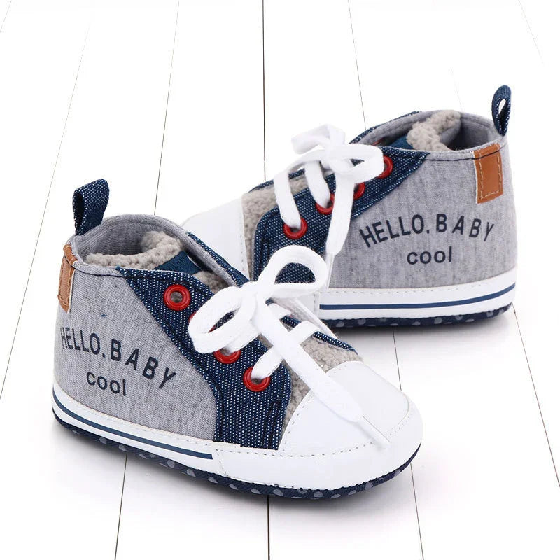 Gray and blue baby sneakers with white laces and text 'HELLO BABY cool' on white wooden floor