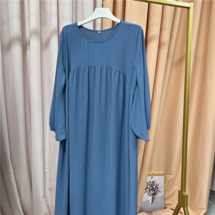Blue long sleeve loose-fit dress hanging on white hanger against beige curtains