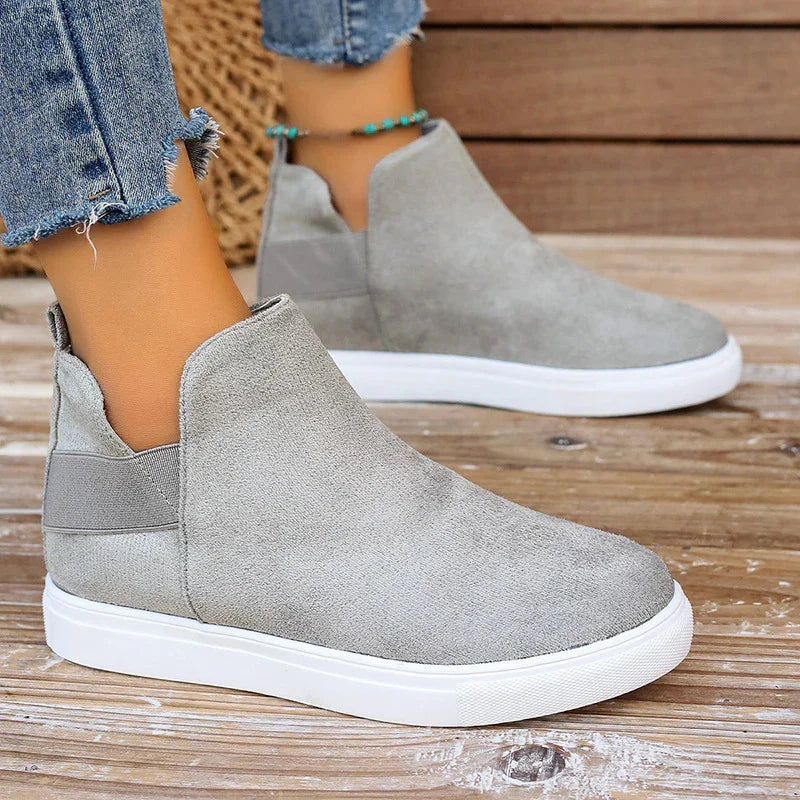 Gray suede slip-on sneakers with white sole worn with cropped frayed hem jeans and turquoise ankle bracelet on wooden floor