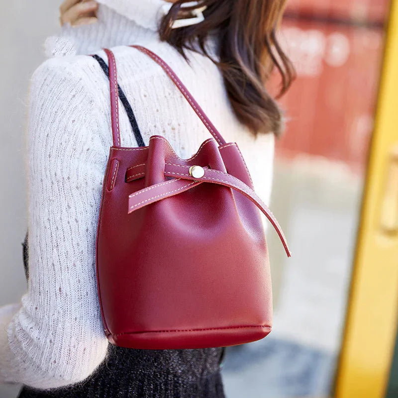 Woman wearing a white sweater and black dress carrying a small red leather bucket bag with a drawstring closure