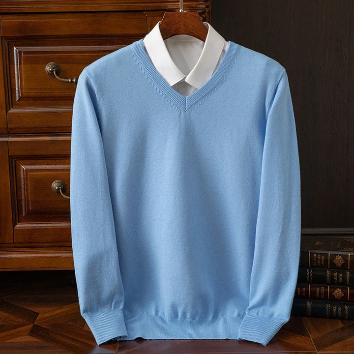 Light blue V-neck sweater layered over white collared shirt, displayed on wooden hanger with books and wooden drawers background