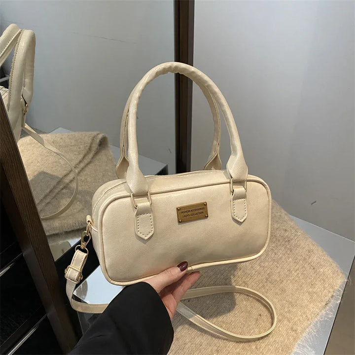 Beige small handbag with double handles and shoulder strap, displayed on table with mirror reflection