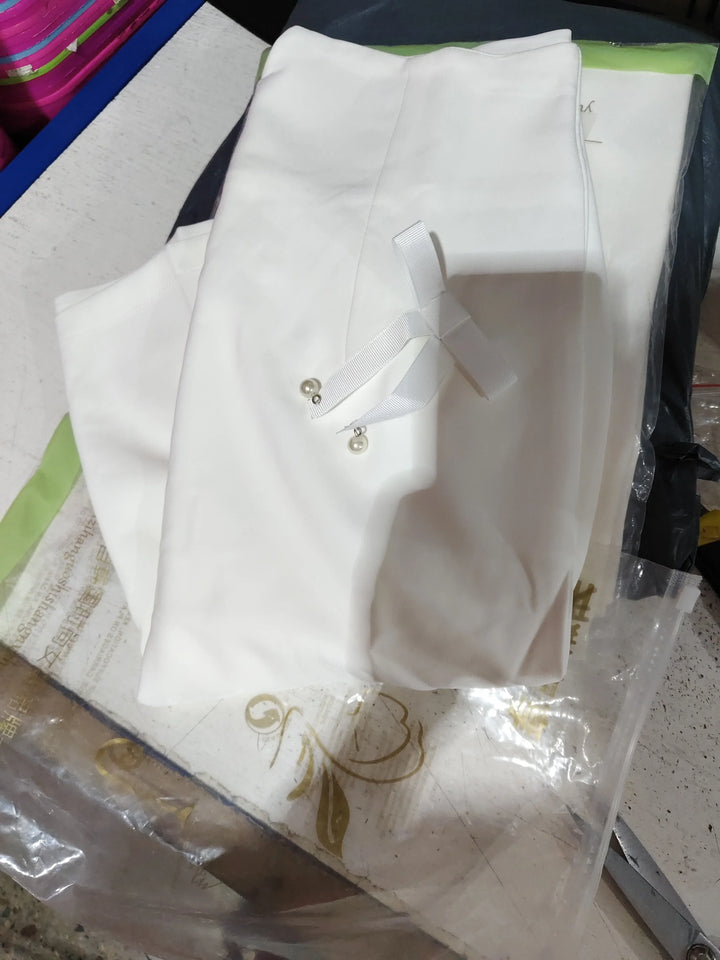 White fabric folded with white ribbon and pearl pins on textured surface with packaging materials