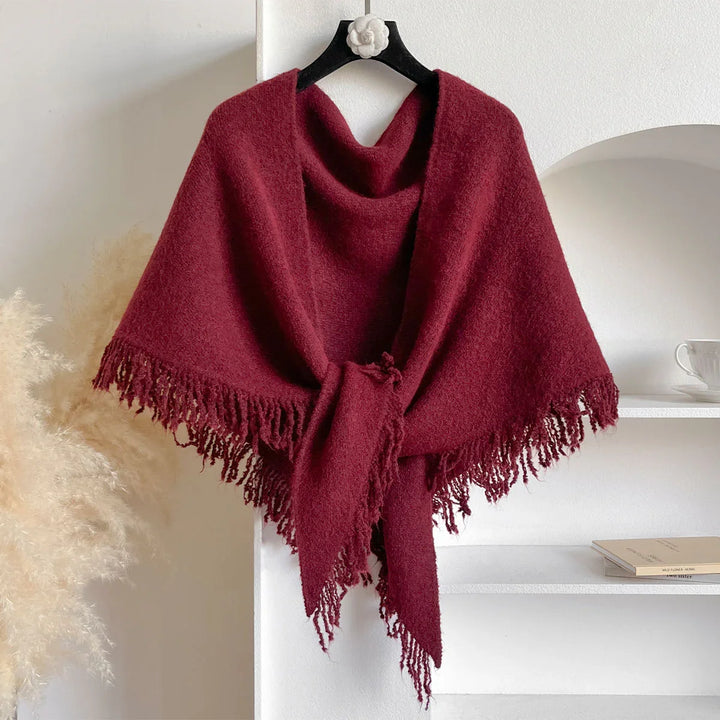 Burgundy wool shawl with fringe hanging on a black hanger against white wall and shelf