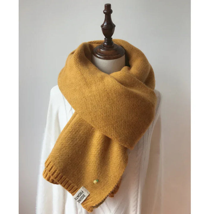Mustard yellow knitted wool scarf on mannequin wearing white sweater