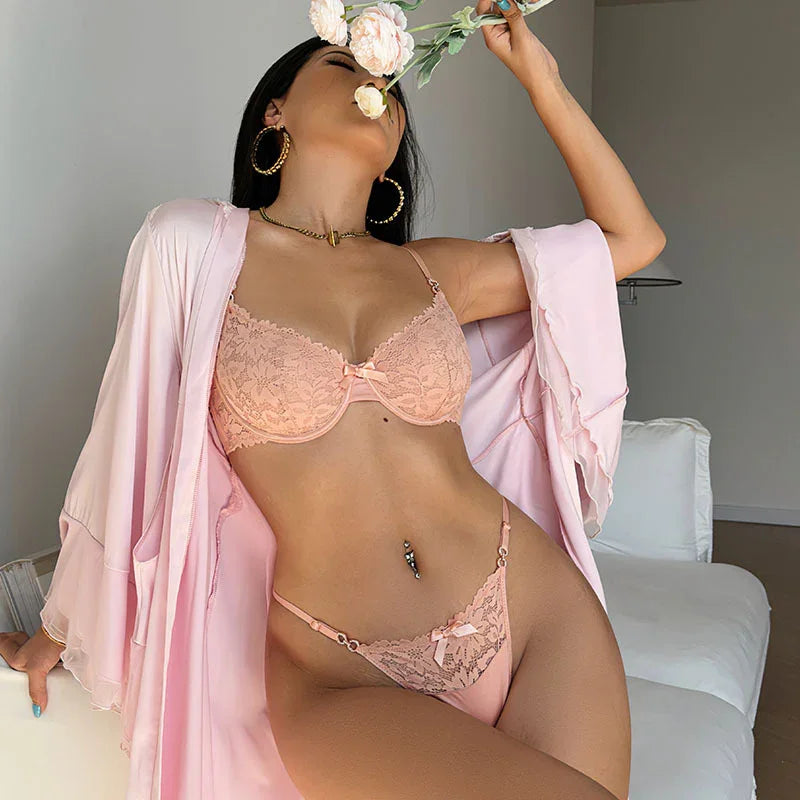 Woman in pink lace lingerie and robe posing indoors holding a flower near her face