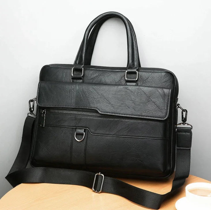 Black leather briefcase with handles and adjustable shoulder strap on wooden table near coffee cup