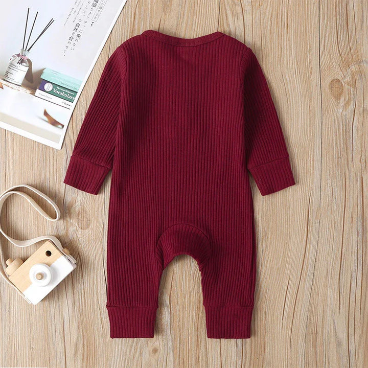 Maroon ribbed long-sleeve baby romper on wooden surface with toy camera and book