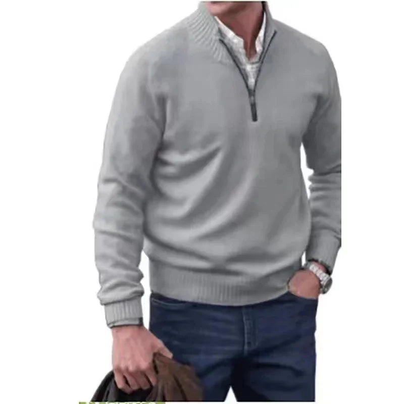 man wearing gray quarter-zip sweater over white shirt with blue jeans holding brown jacket