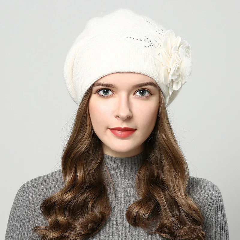 Young woman with long wavy brown hair wearing a white beret with flower detail and grey ribbed sweater