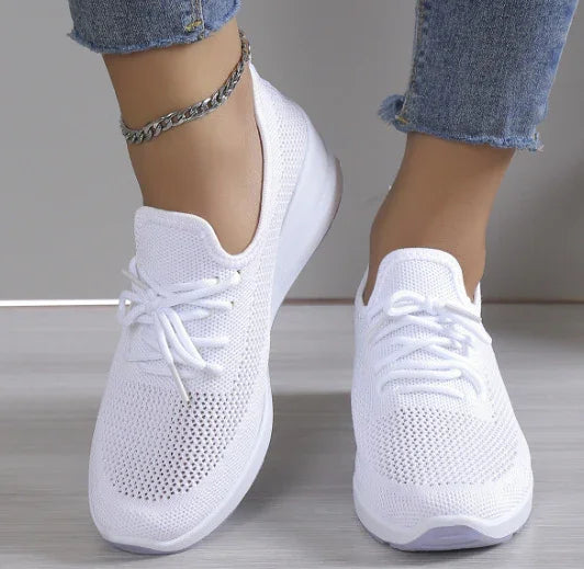 White knitted mesh athletic sneakers worn with blue frayed hem jeans and silver ankle bracelet