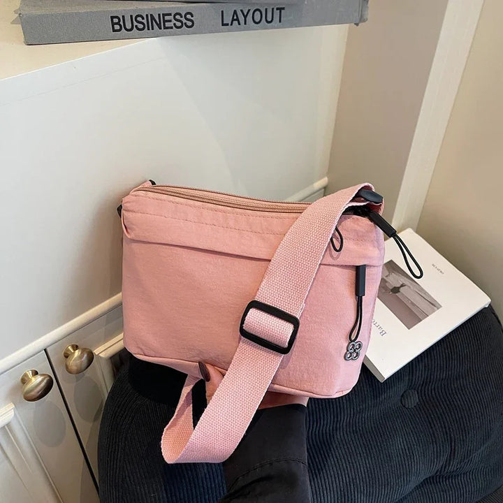 Pink canvas crossbody bag with adjustable strap on black chair near white cabinet and book