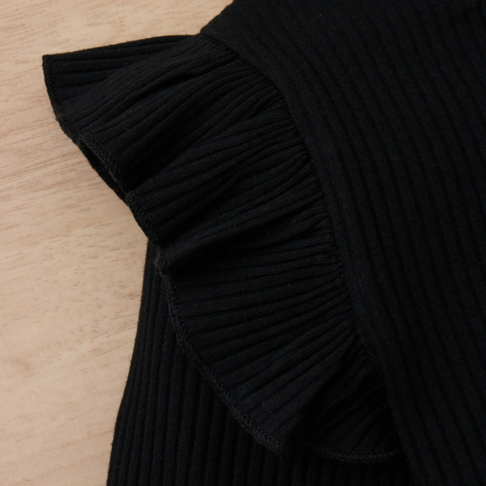 Close-up of black ribbed fabric with a ruffled edge on a wooden surface