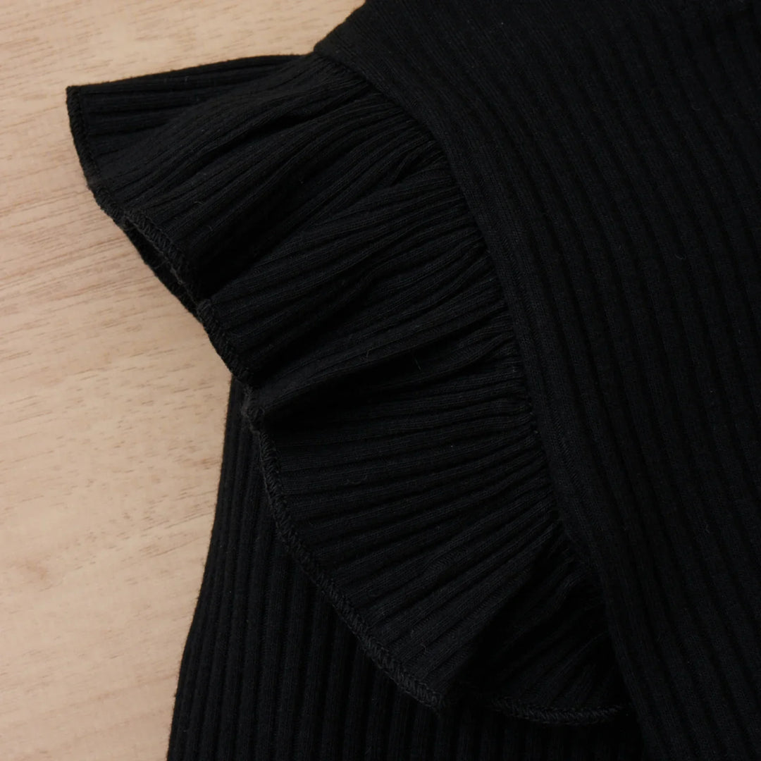 Close-up of black ribbed fabric with a ruffled edge on a wooden surface