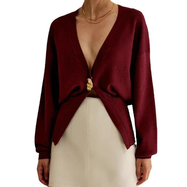 Woman wearing deep burgundy cardigan with gold button and beige skirt, accessorized with gold chain necklace