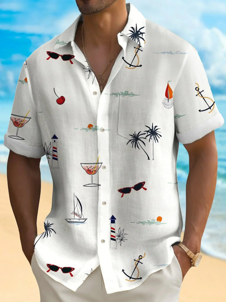 Man wearing white short-sleeve beach shirt with tropical prints of anchors, palm trees, sailboats, and cocktails
