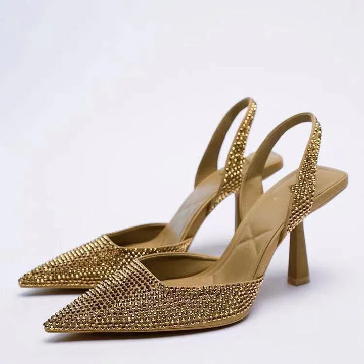 Pair of gold high heel slingback shoes adorned with small studs on a white background