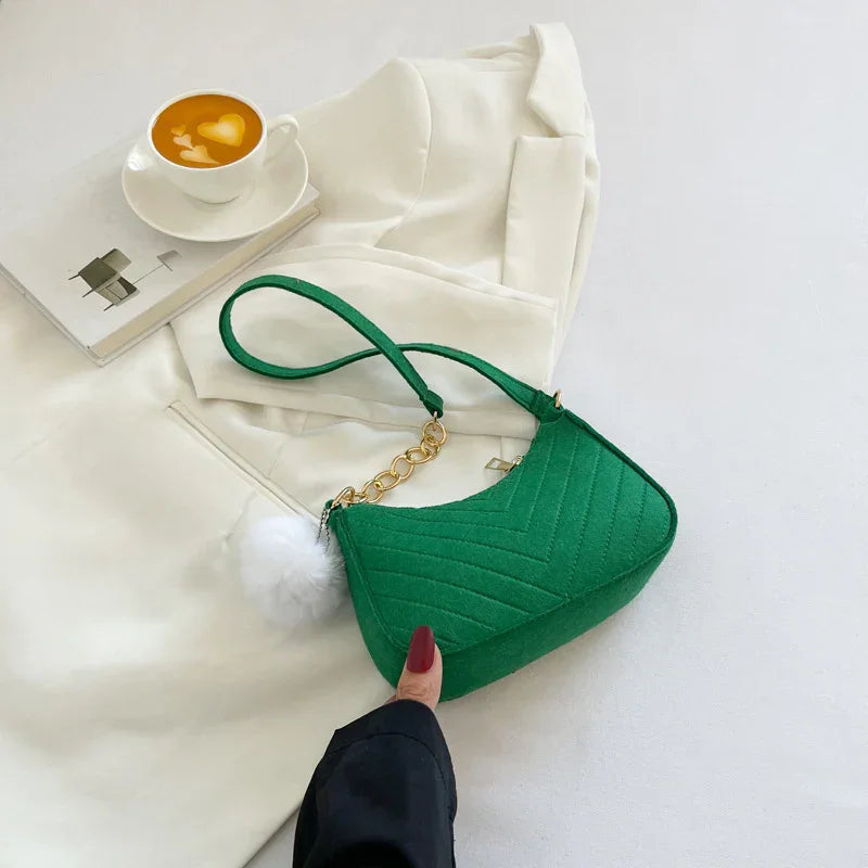 Green quilted handbag with gold chain and white pompom on white clothing next to cappuccino latte art