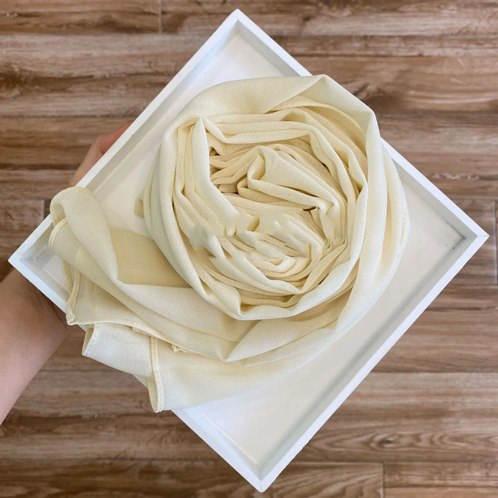 Hand holding a white square tray with a neatly folded cream fabric resembling a rose on wooden floor