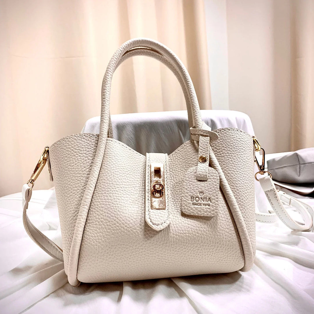 Creamy white textured leather Bonia handbag with gold clasp and adjustable strap on white fabric