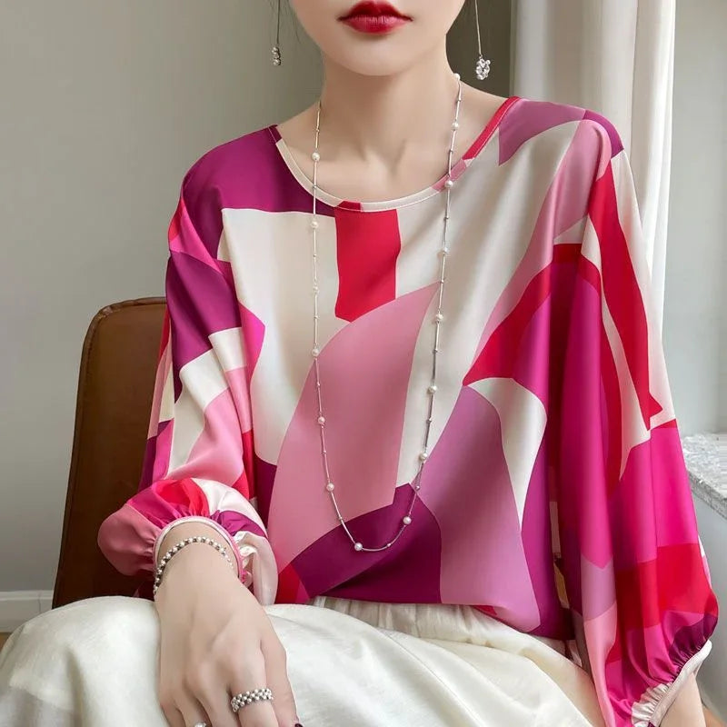 Woman wearing a colorful geometric print blouse in shades of pink and red with pearl necklace and ring