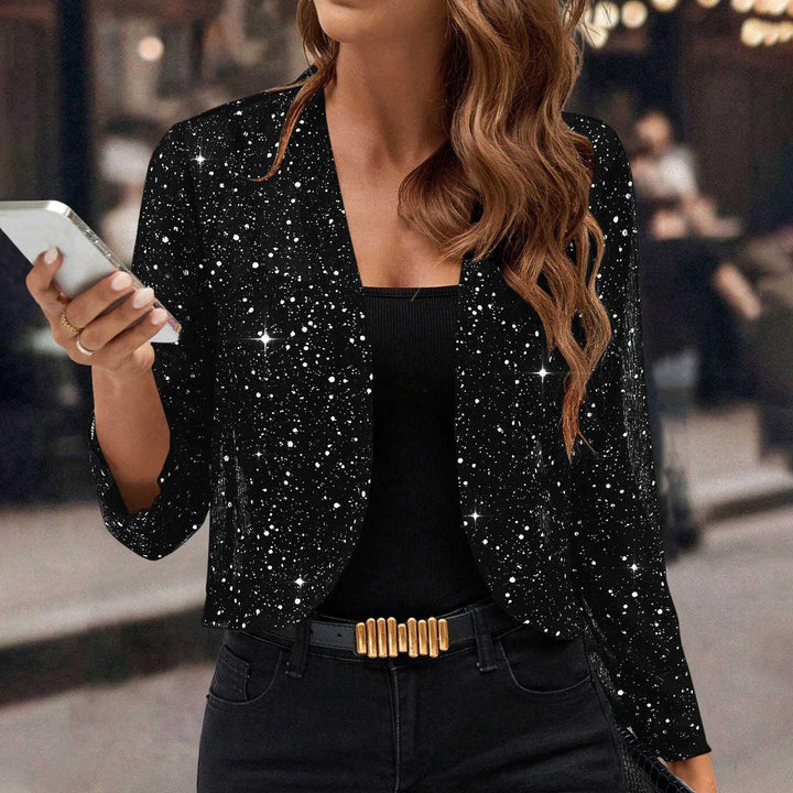Woman wearing black sparkling galaxy print blazer with black top and jeans, holding white smartphone