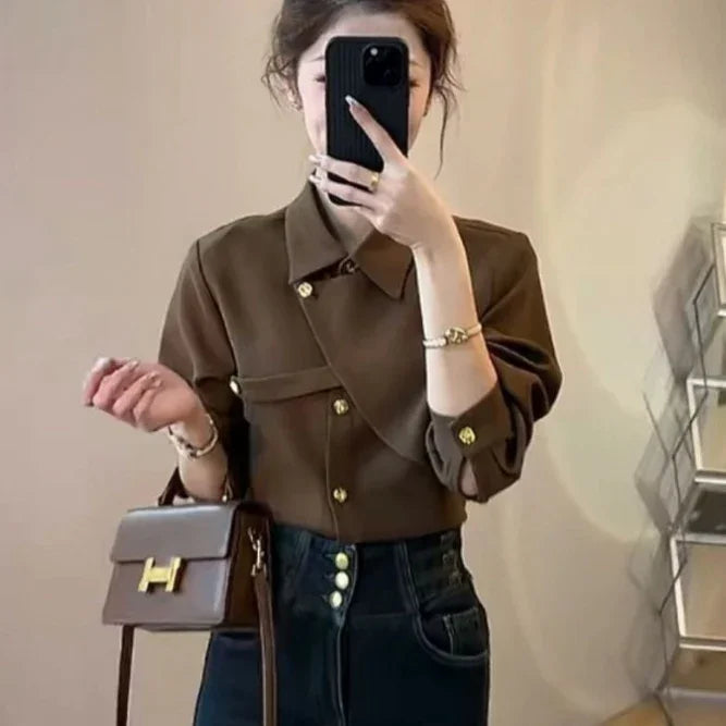 Woman taking mirror selfie wearing brown buttoned blouse, high-waisted dark jeans, and carrying brown handbag