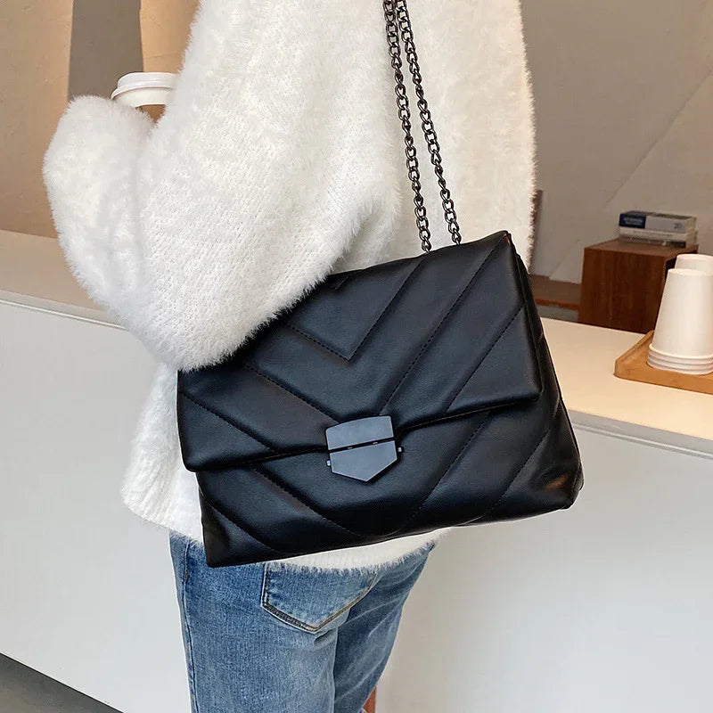 Woman wearing white fuzzy sweater and blue jeans with black quilted leather shoulder bag indoors