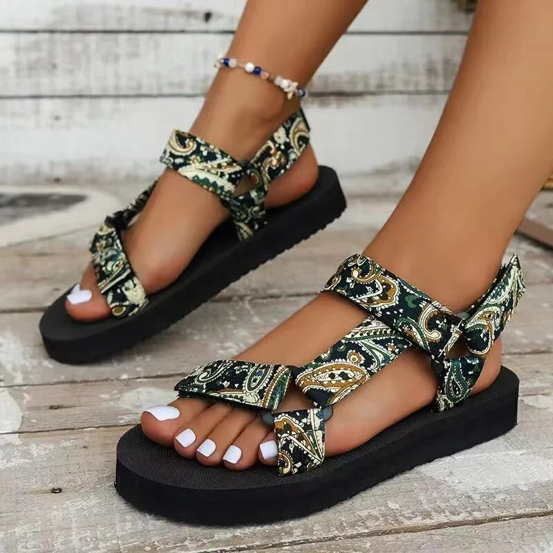 Close-up of feet wearing black platform sandals with green paisley fabric straps and white nail polish