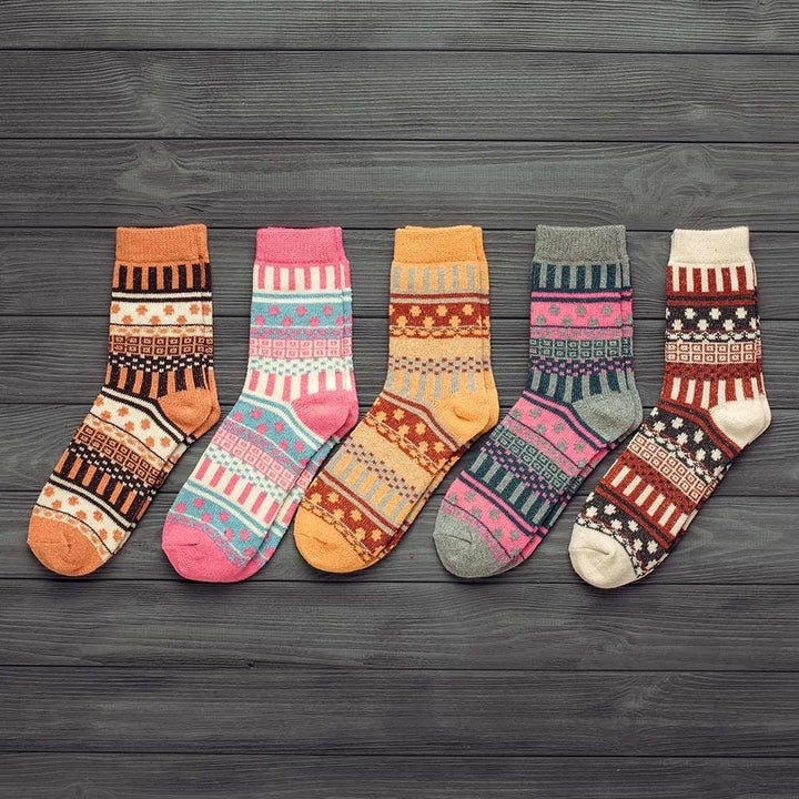 Five colorful patterned knit socks in orange, pink, yellow, gray, and cream on dark wooden background