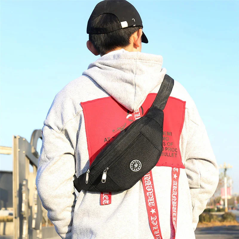 Man wearing a gray hoodie with red graphic and black crossbody sling bag outdoors