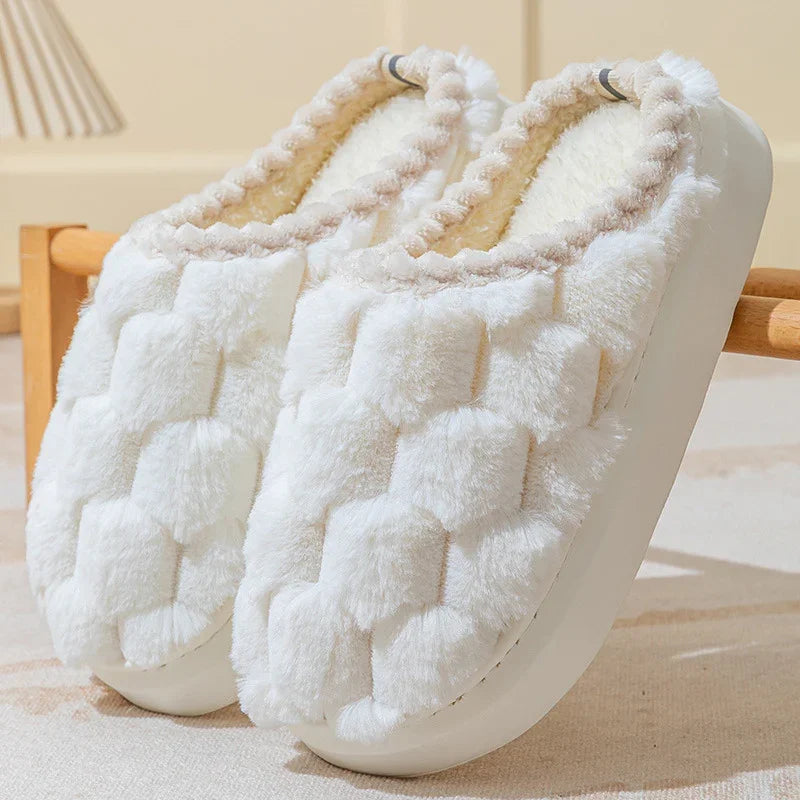 Pair of white plush indoor slippers with textured soft fur and cushioned soles on a beige surface
