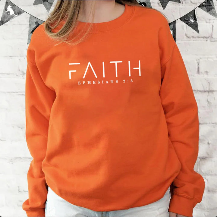 Person wearing orange sweatshirt with Faith Ephesians 2:8 quote against white brick wall
