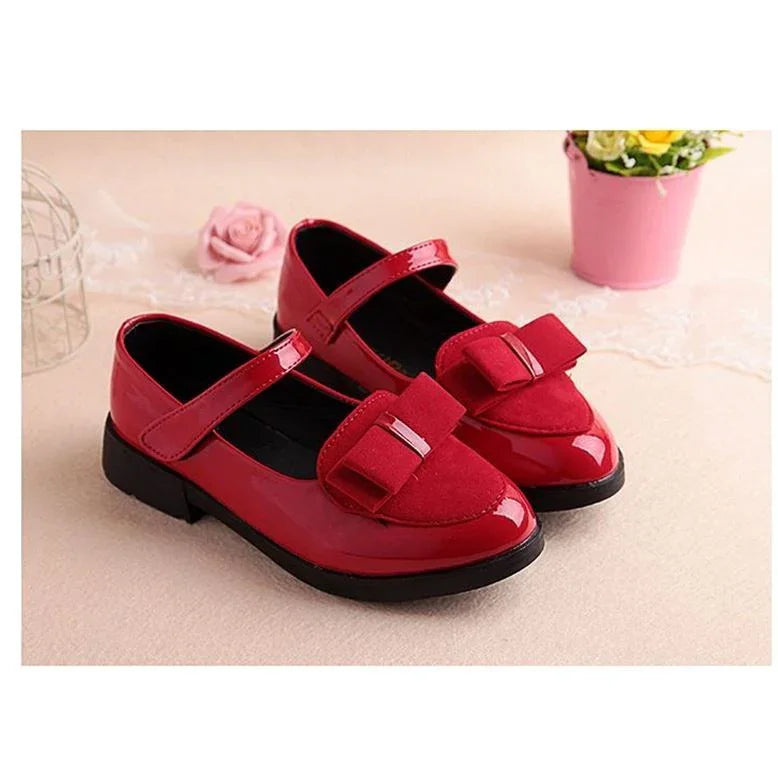 Red girls' Mary Jane shoes with decorative bows and black soles on beige background