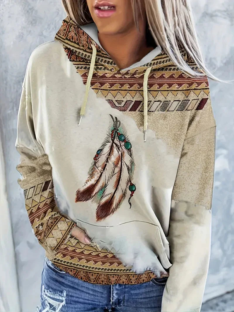 Woman wearing beige hoodie with tribal patterns and print of feathers with turquoise beads, paired with distressed blue jeans