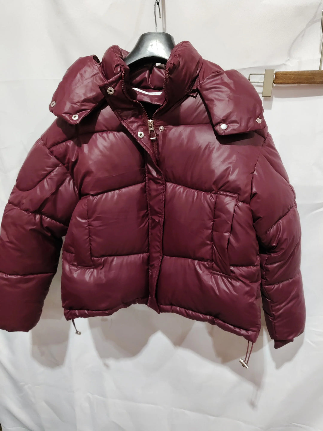 Burgundy puffer jacket with zipper and snap buttons hanging on black hanger