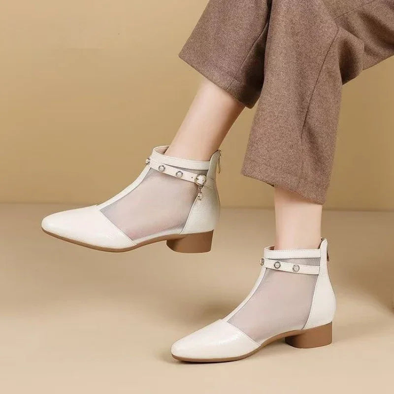 Pair of white mesh ankle boots with low brown heels and studded straps on a model with brown pants