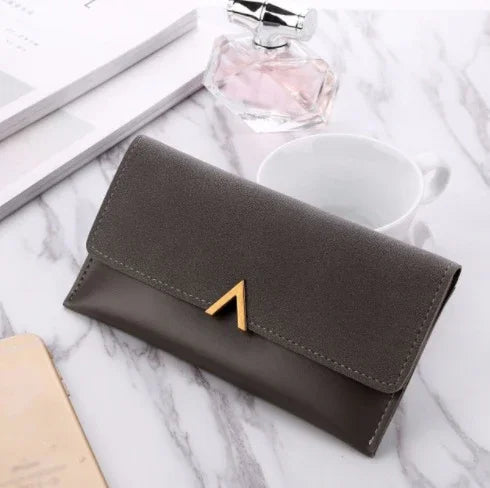 Stylish gray leather wallet with gold triangular clasp on marble surface with perfume and white cup