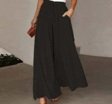 Woman wearing black wide-leg high-waist trousers with side pockets, white top, and holding brown clutch