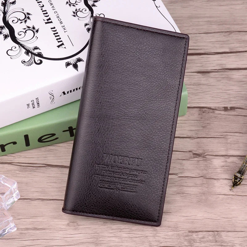 Black leather long wallet on wooden surface with decorative books and accessories