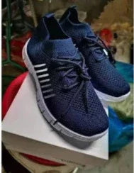 Pair of navy blue athletic sneakers with white soles and stripes on white box in indoor setting