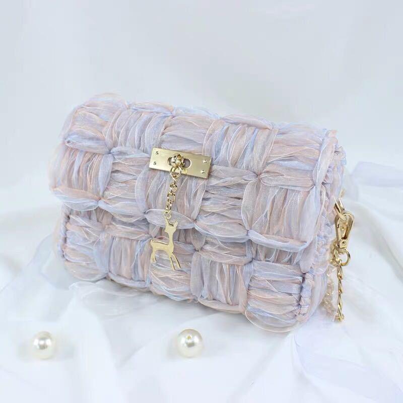 Elegant woven pink handbag with gold deer charm and chain detail on white fabric background