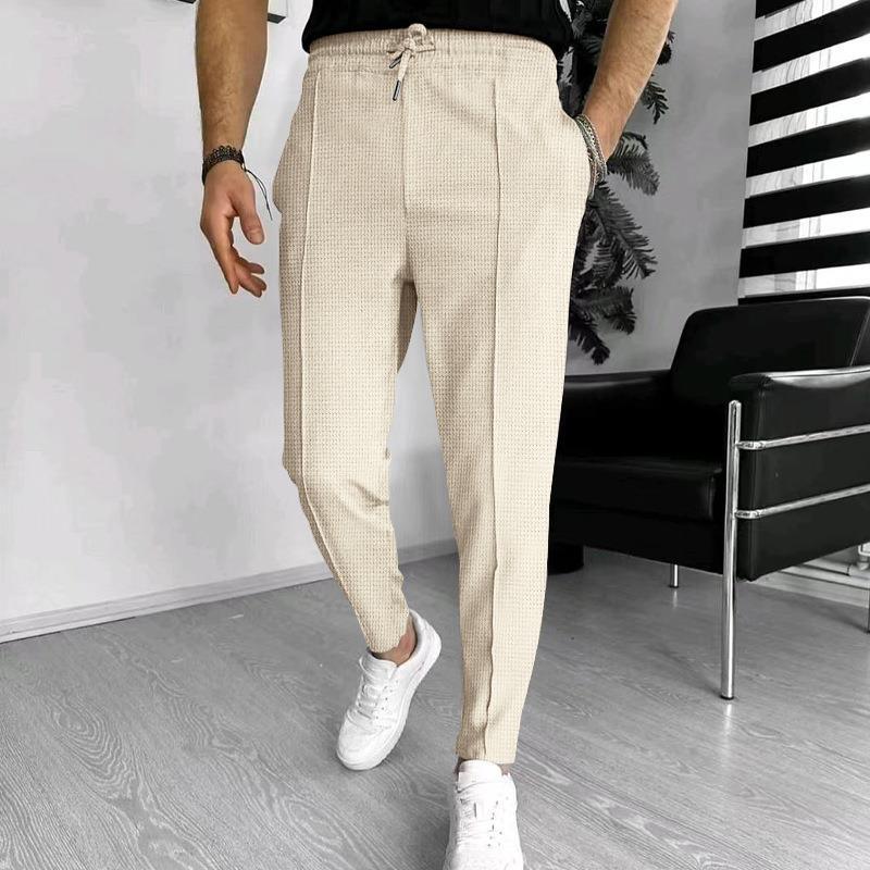 Man wearing beige textured casual pants with drawstring and white sneakers in modern room