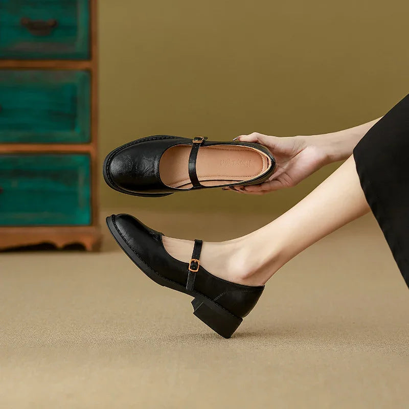 Woman wearing and holding black leather Mary Jane shoes with low block heel on beige carpet