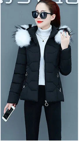 Woman wearing black padded winter jacket with white fur hood, black pants, sunglasses, holding smartphone