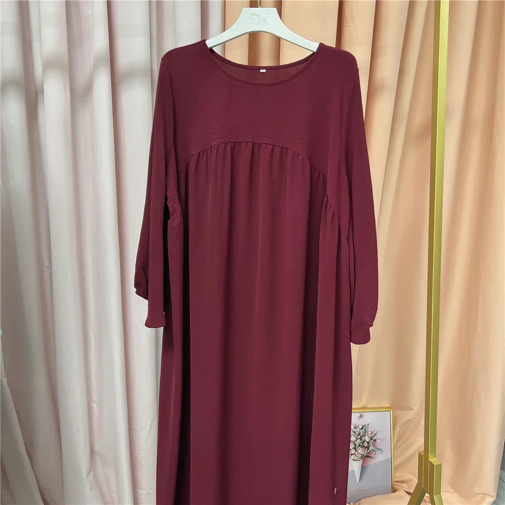 Maroon long-sleeve loose dress hanging on white hanger with curtains and gold clothing rack