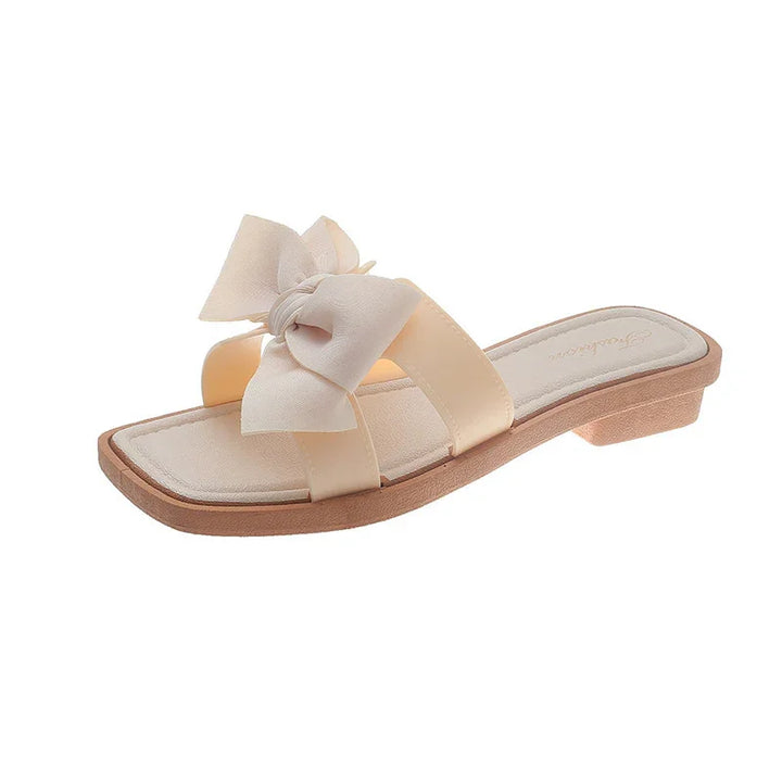 Beige women's slide sandal with large soft fabric bow and low wooden heel