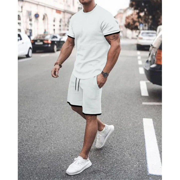Man walking on street wearing white t-shirt and shorts with black trim, white sneakers, casual summer outfit