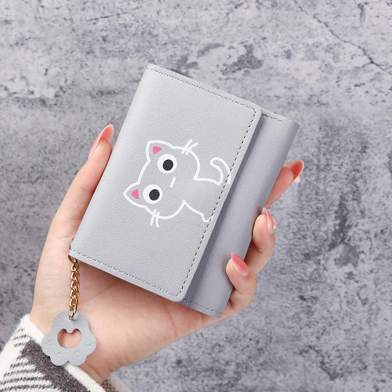 Hand holding gray wallet with cute white cat design and flower charm on chain